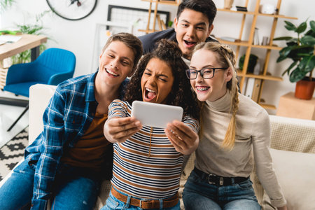 happy multiethnic teenagers taking selfie with smartphone at home