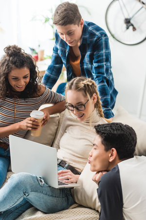 group of multicultural teens looking at laptop at homeの写真素材