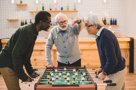group of handsome senior friends playing table football at bar