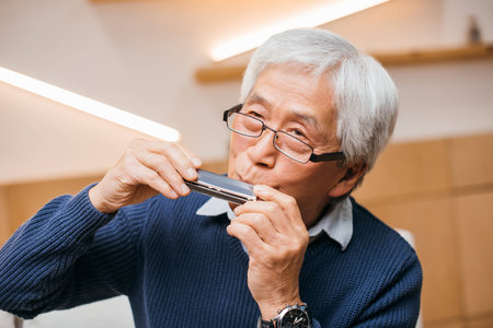portrait of happy senior asian man playing harmonica