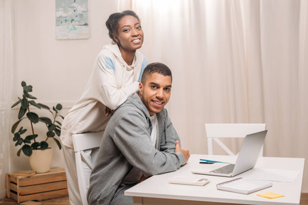 happy african american couple with laptop looking at camera at homeの写真素材