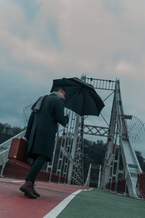 bottom view of handsome middle aged man with umbrella and luggage walking by pedestrian bridgeの写真素材