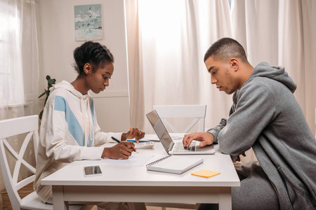 side view of african american couple using laptop and calculating something at home