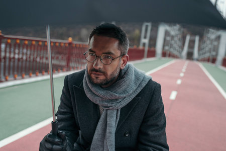 handsome adult man with umbrella walkign by pedestrian bridgeの写真素材