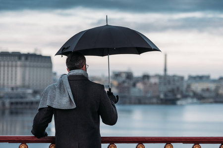 back view of lonely man with umbrella standing on bridgeの写真素材