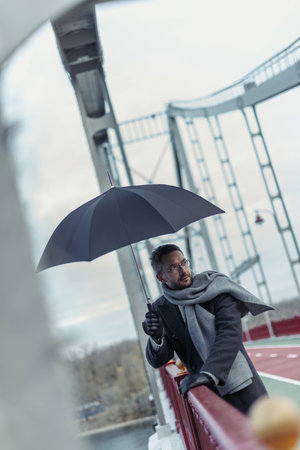 stylish adult man in scarf with umbrella on bridgeの写真素材
