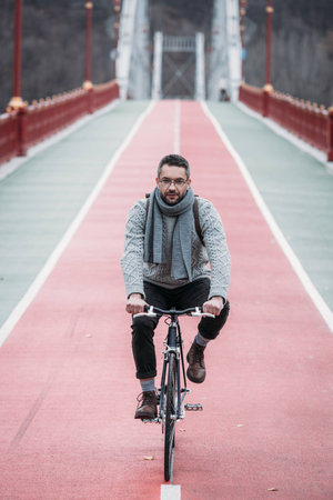 handsome adult man in sweater riding bicycle on pedestrian bridgeの写真素材