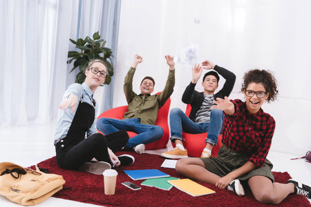 young happy students sitting and throwing paper in camera