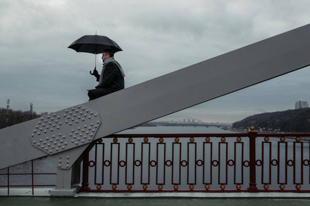 lonely man with umbrella sitting on bridge constructionの写真素材