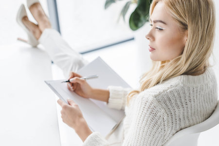 attractive pensive businesswoman in white clothes with paperworkの写真素材