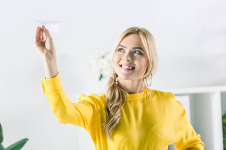 cheerful businesswoman in yellow blouse holding paper planeの写真素材
