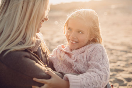 happy mother hugging her daughter on sandy beach with backlitの写真素材