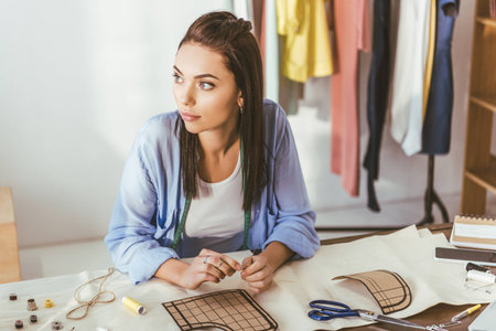 thoughtful seamstress sitting at working table and looking awayの写真素材