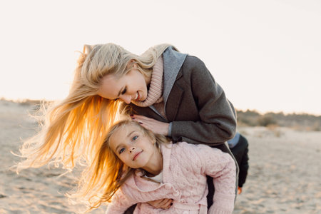 happy mother embracing her daughter on seashore with backlitの写真素材