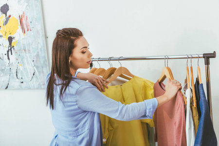 attractive designer looking at shirts on hangersの写真素材