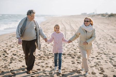 grandparents holding hands with granddaughter while walking on seashore in autumn