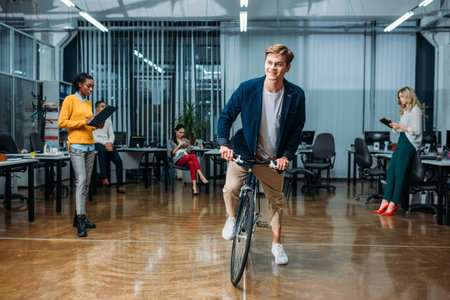 happy young businessman riding bike at modern office while his colleagues working