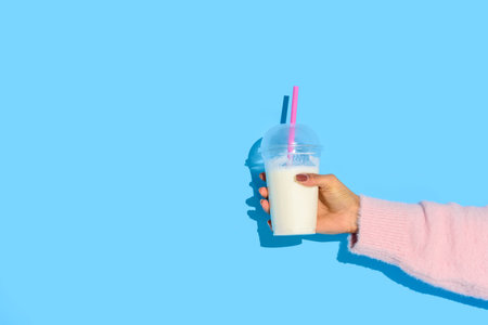 partial view of african american woman holding glass of milk with straw against blue backgroundの写真素材
