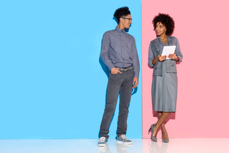 Young african amercian businessman standing by girl with tablet in hands on pink and blue backgroundの写真素材