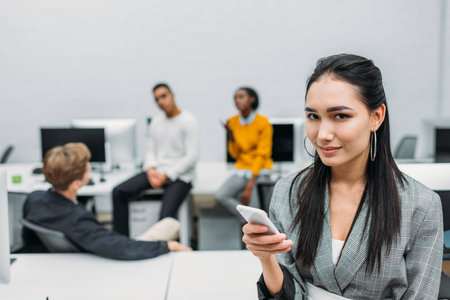 young asian businesswoman using smartphone with blurred partners on backgroundの写真素材