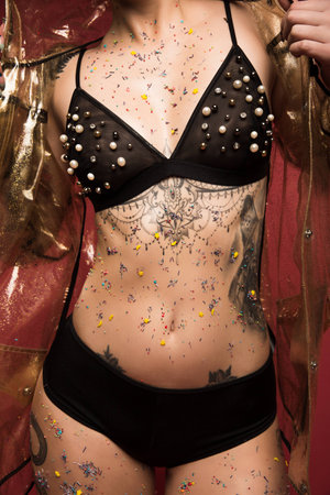 cropped image of female body with tattoos in lingerie and raincoat infront of red backgroundの写真素材