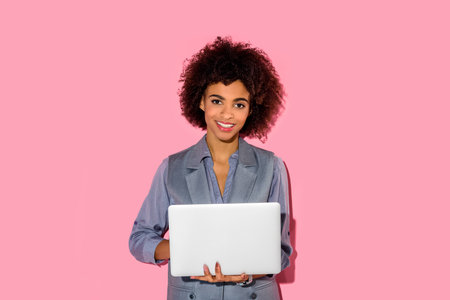 Young african amercian smiling businesswoman holding laptop on pink backgroundの写真素材