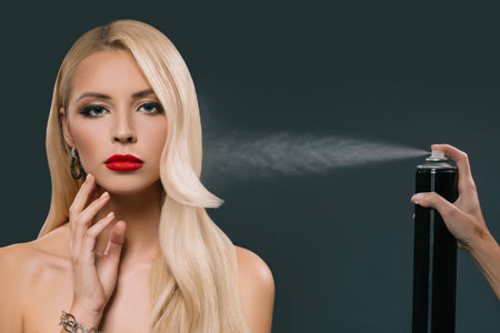 pretty beautiful blonde hair girl with hand using spray isolated on blackの写真素材