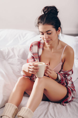 gorgeous elegant girl in checkered shirt drinking coffee in bed in the morningの写真素材