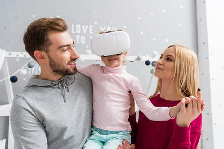 parents looking at little daughter while she using virtual reality headsetの写真素材