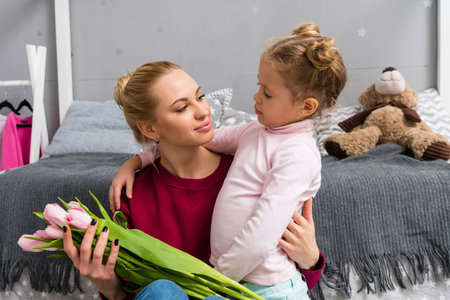 adorable little daughter presenting tulips bouquet for mother on mothers dayの写真素材