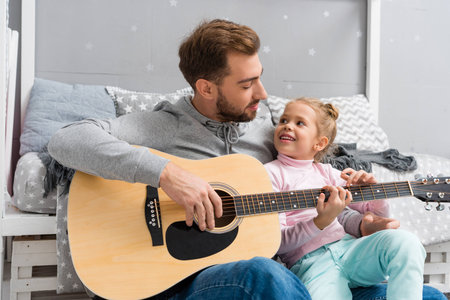 father playing guitar for daughter on floor of kid bedroomの写真素材