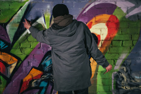 back view of man painting graffiti with aerosol paint on wall at nightの写真素材
