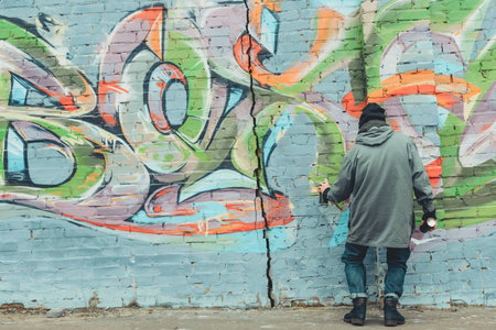 back view of street artist painting colorful graffiti on wallの写真素材