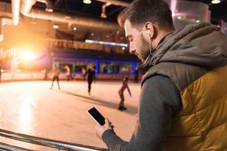 handsome young man in earphones using smartphone with blank screen on rink