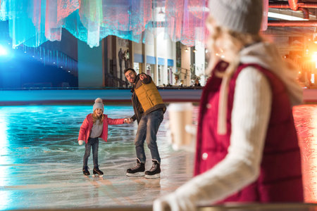 happy father and daughter holding hands and pointing with finger at young woman drinking coffee on foregroundの写真素材