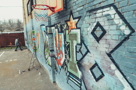 man painting colorful graffiti on wall with basketball hoopの写真素材
