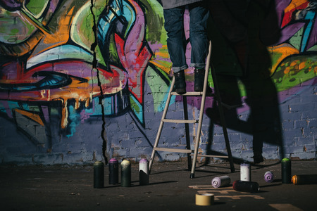 cropped view of standing on ladder and painting colorful graffiti at nightの写真素材