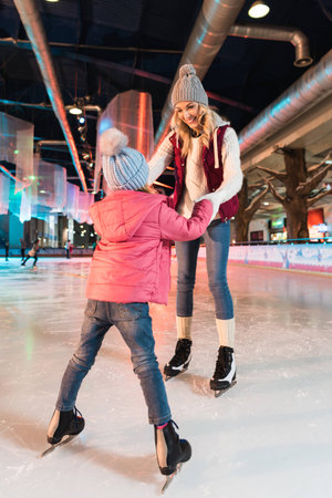 happy mother and daughter holding hands and looking at each other on skating rinkの写真素材