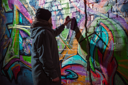 street artist painting graffiti with aerosol paint on wall at nightの写真素材