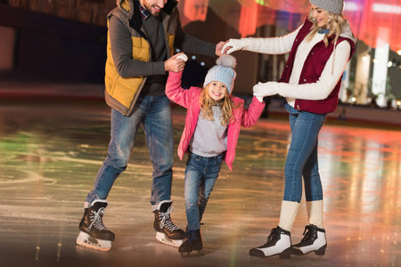 cropped shot of happy parents teaching adorable little daughter skating on rinkの写真素材