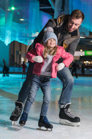 happy father hugging adorable little daughter on skating rinkの写真素材