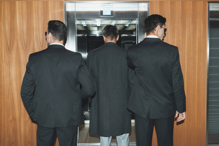 back view of bodyguards and businessman standing at elevator