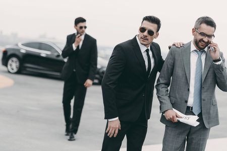happy businessman walking with bodyguards and talking by smartphoneの写真素材