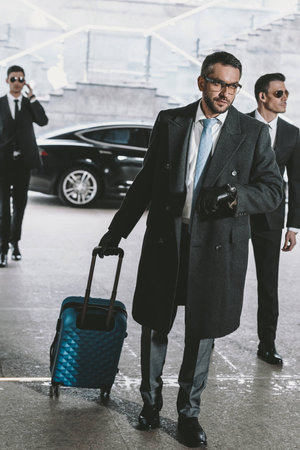 handsome businessman walking with travel bag from car and looking at watchの写真素材