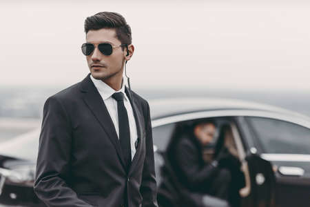 bodyguard reviewing territory while businessman going out from carの写真素材