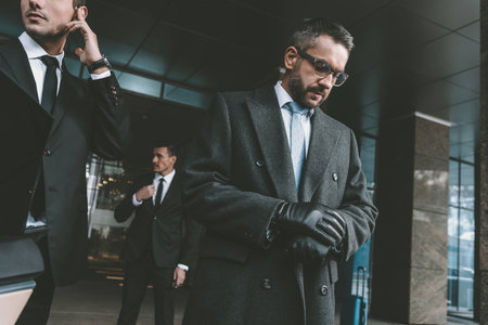 businessman looking at watch and standing with bodyguardsの写真素材