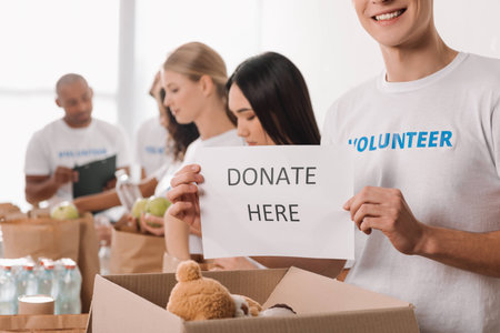 cropped shot of volunteer holding charity placard with blurred colleagues working on backgroundの写真素材