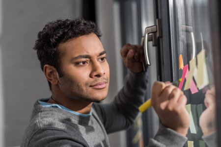 young man making notes on stickers at window