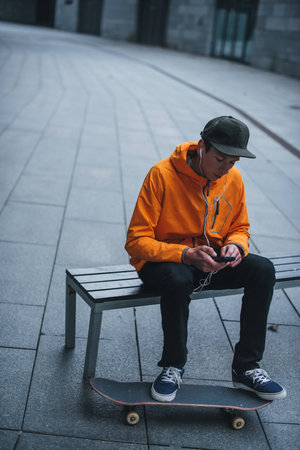 skateboarder sitting on bench and listening music with smartphoneの写真素材