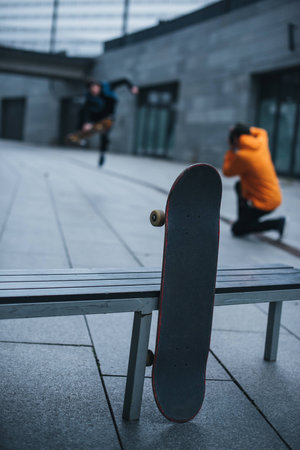 skateboarders taking photos of tricks with skateboard leaning at bench on foregroundの写真素材
